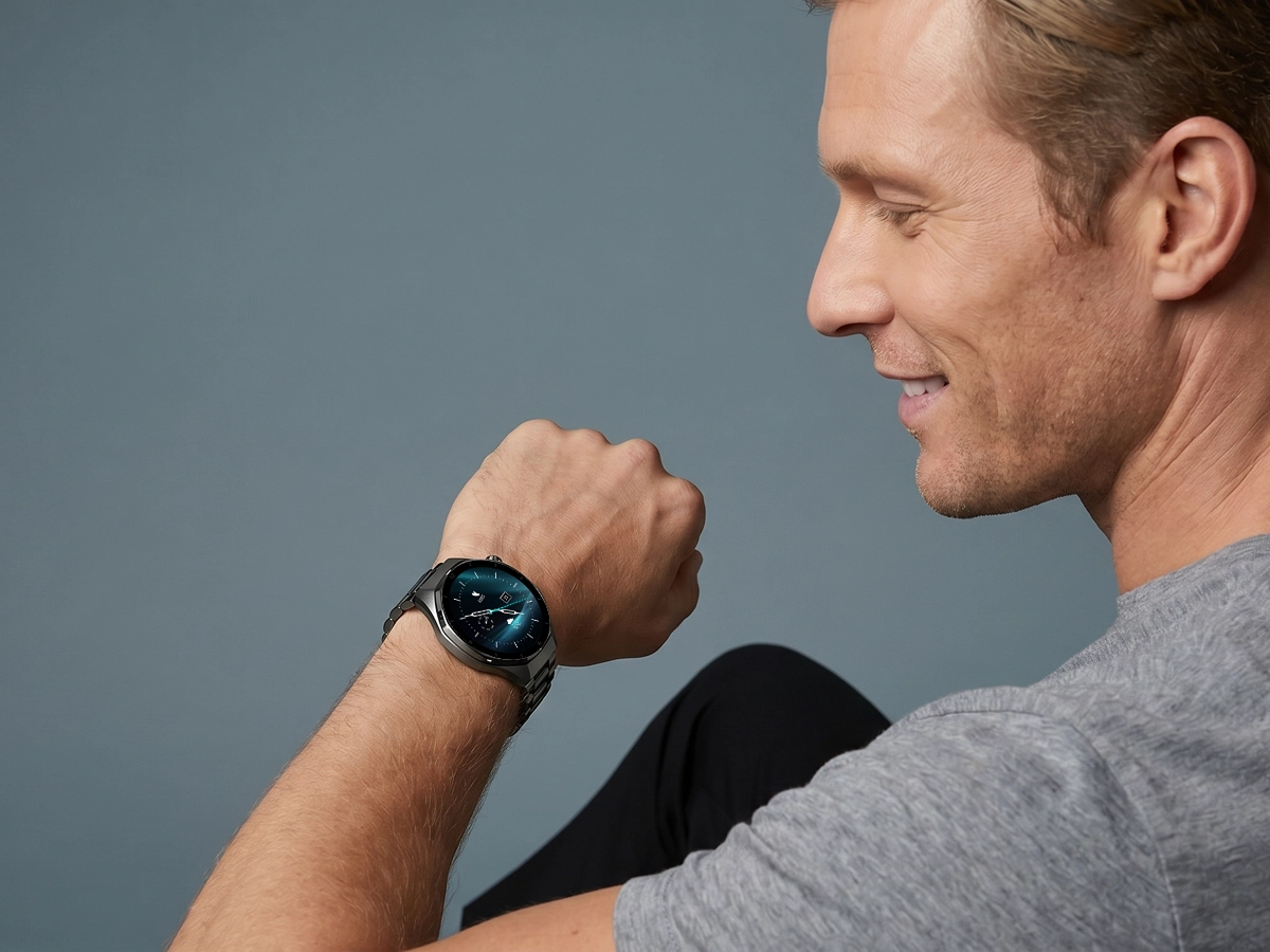 Mężczyzna w szarej koszulce prezentuje smartwatch męski Z-Base z wyraźnym ekranem na nadgarstku.