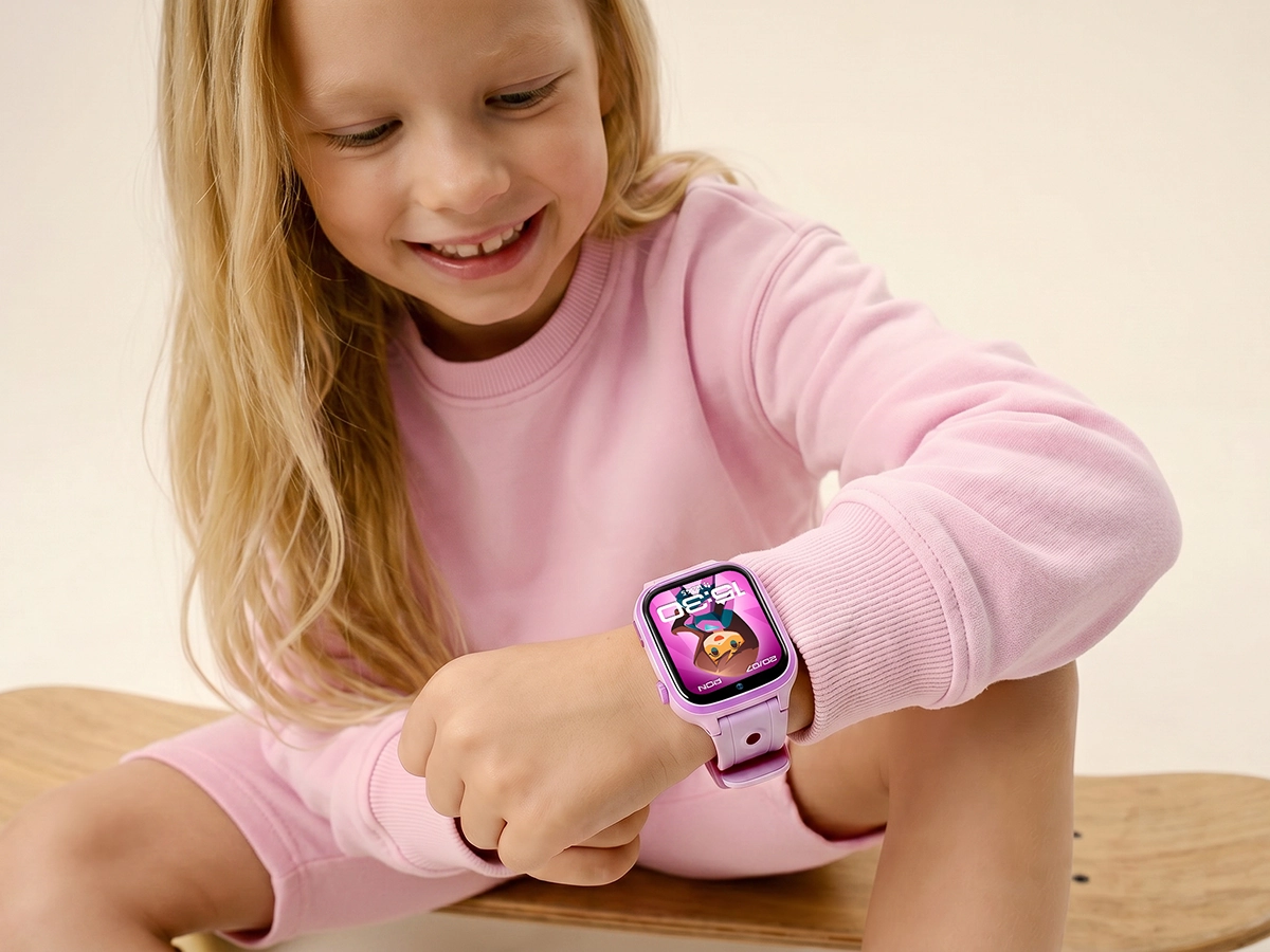 Uśmiechnięta dziewczynka w różowej bluzie siedzi na deskorolce i patrzy na smartwatch dziecięcy Besti.