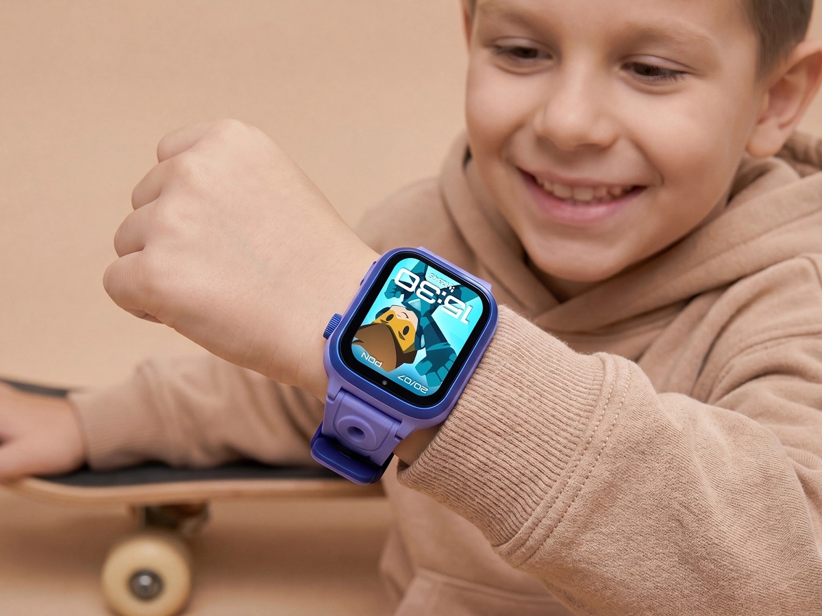 Uśmiechnięty chłopiec w beżowej bluzie prezentuje niebieski smartwatch dziecięcy Bro podczas zabawy.