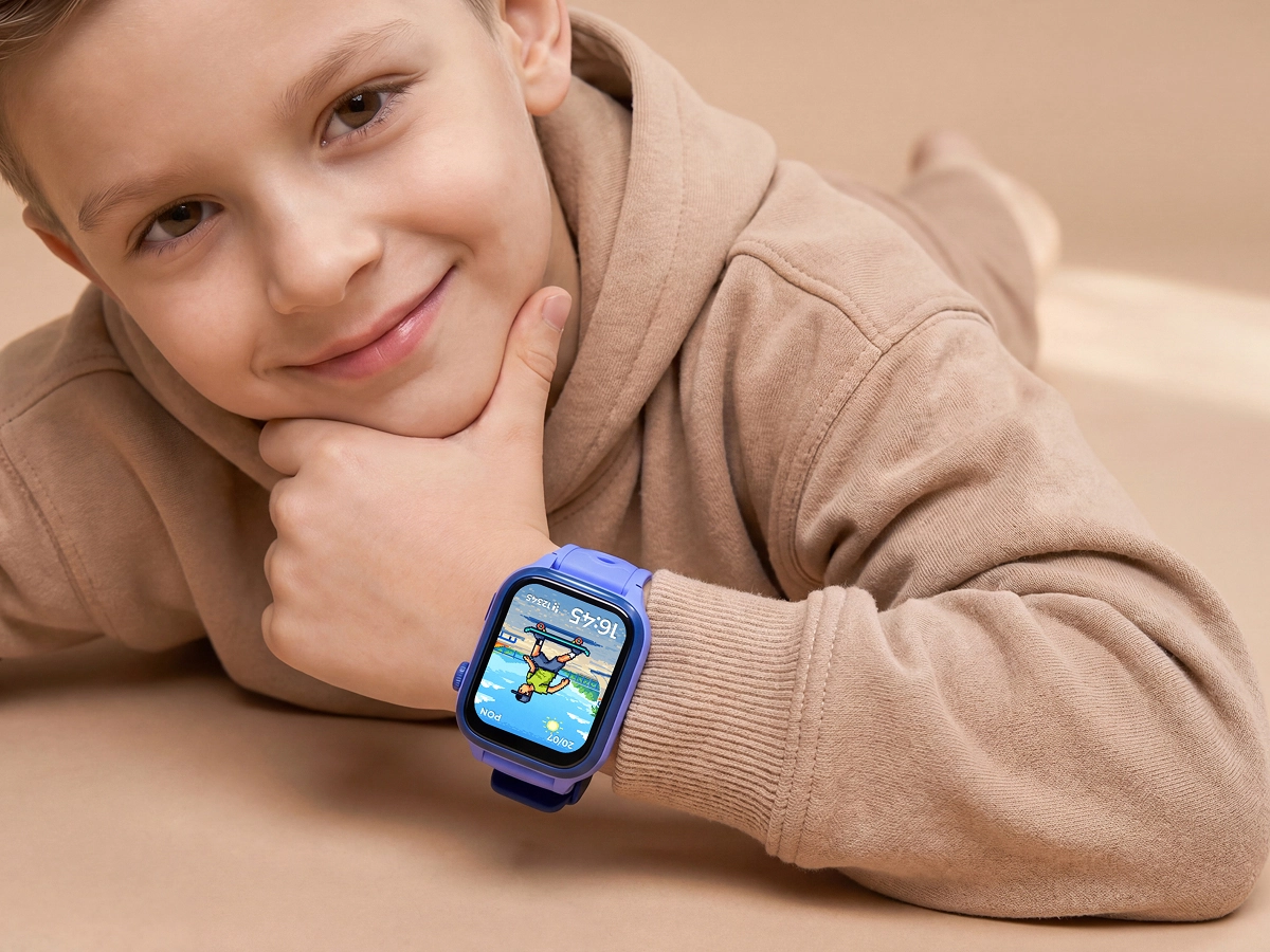 Uśmiechnięty chłopiec w beżowej bluzie opiera się na dłoni i pokazuje niebieski smartwatch dziecięcy Bro.