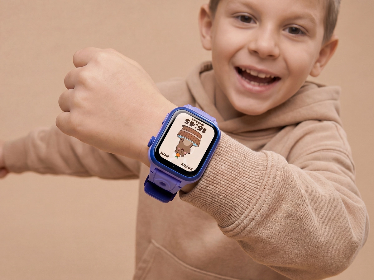 Podskakujący chłopiec w beżowej bluzie pokazuje smartwatch dziecięcy Bro z niebieskim paskiem i kolorową tarczą.