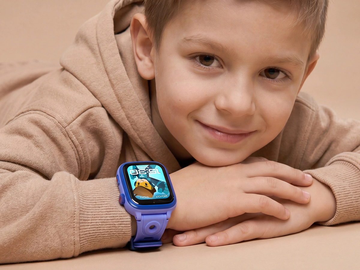 Chłopiec opiera się na dłoniach i pokazuje niebieski smartwatch dziecięcy Bro z kolorową tarczą na nadgarstku.